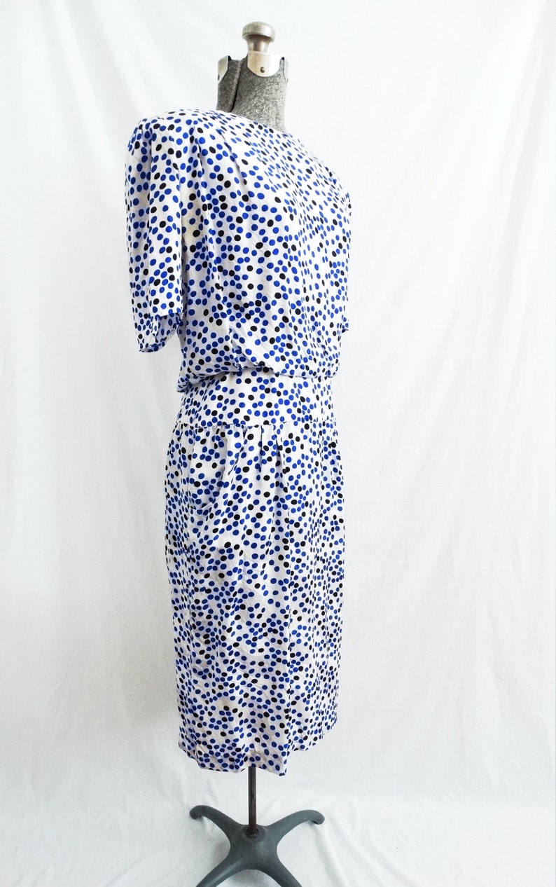 May include: A white dress with a blue and black polka dot pattern. The dress has short sleeves and a fitted bodice. The skirt is slightly flared and falls to the knees.