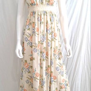 Puede incluir: Un vestido largo de maxi blanco con estampado floral en tonos rosa, azul y verde. El vestido tiene un corpi&ntilde;o ajustado con un ribete de encaje y una falda fluida con un dobladillo con volantes.
