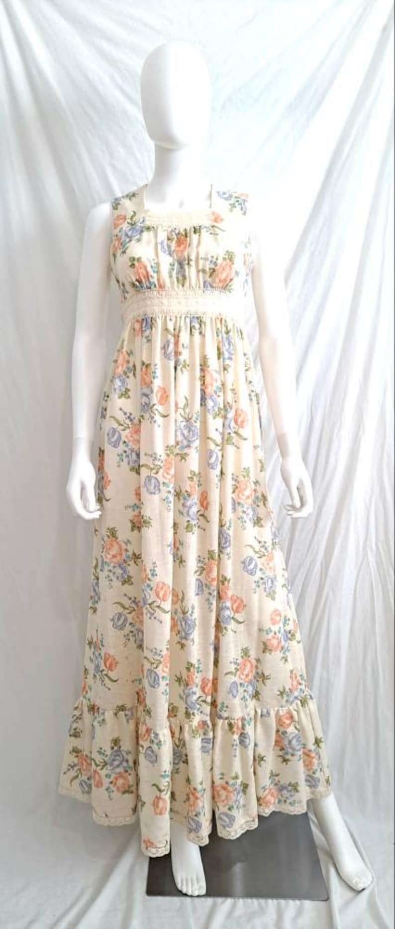 Puede incluir: Un vestido largo de maxi blanco con estampado floral en tonos rosa, azul y verde. El vestido tiene un corpi&ntilde;o ajustado con un ribete de encaje y una falda fluida con un dobladillo con volantes.