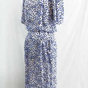 May include: A white dress with a blue and black polka dot pattern. The dress has short sleeves and a fitted bodice. The skirt is slightly flared and falls to the knees.