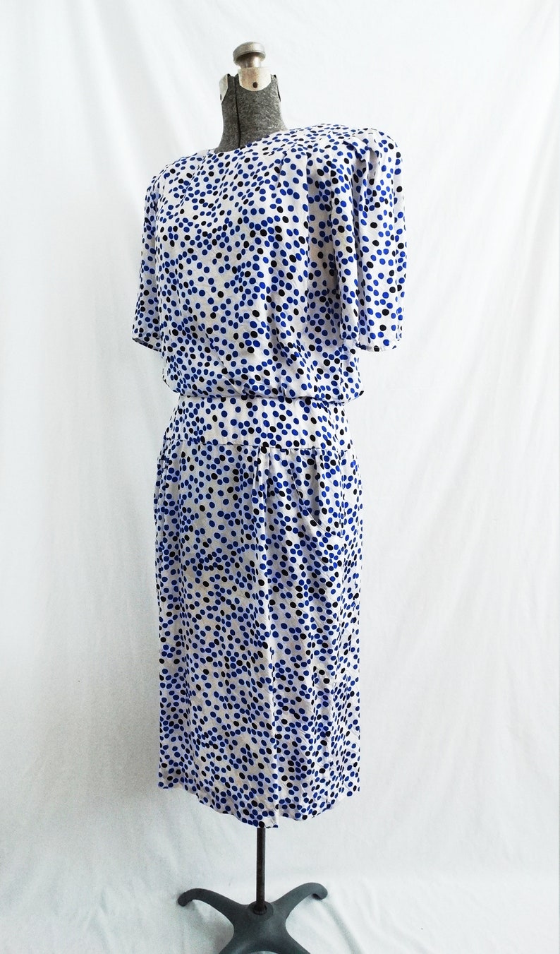 May include: A white dress with a blue and black polka dot pattern. The dress has short sleeves and a fitted bodice. The skirt is slightly flared and falls to the knees.