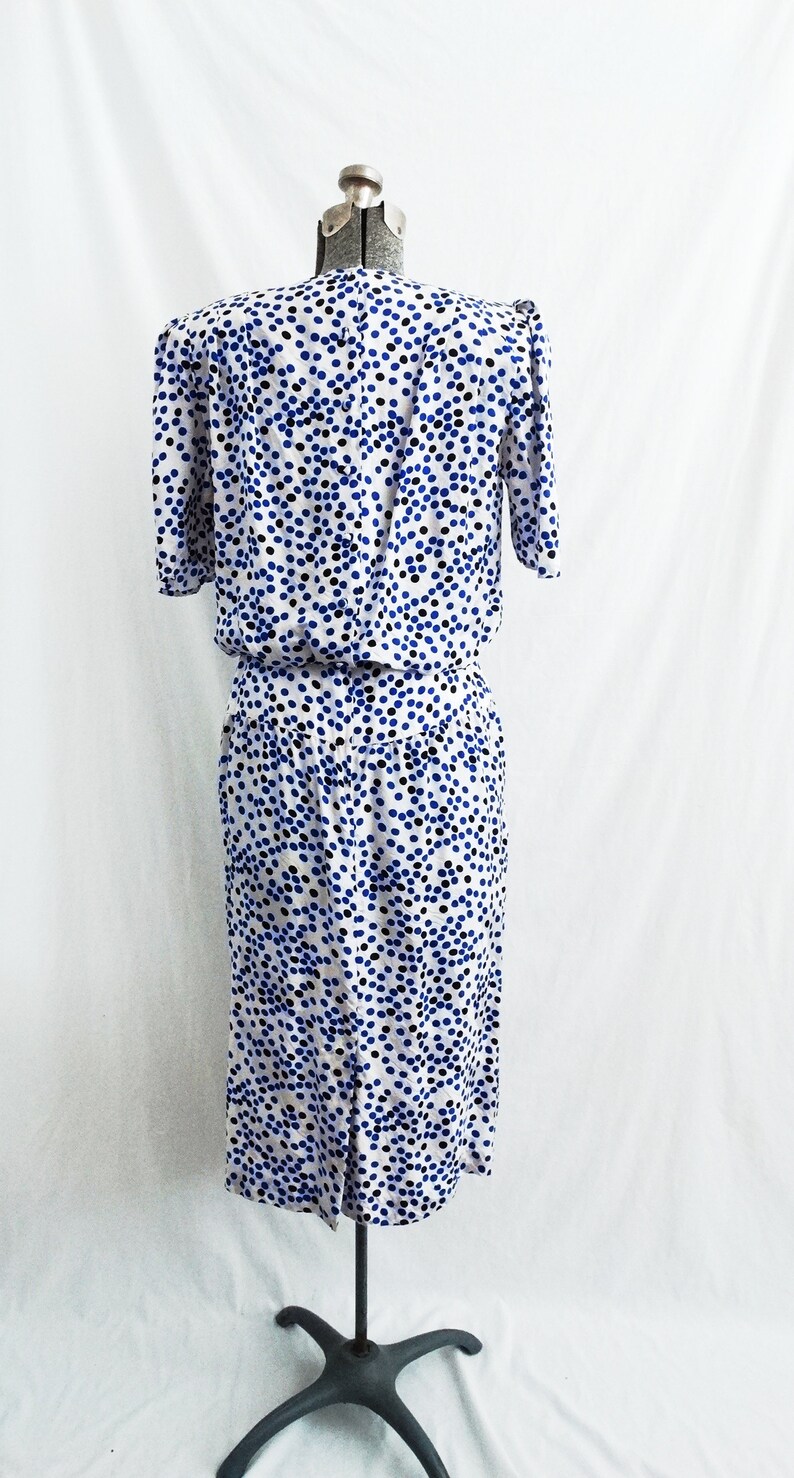 May include: A white dress with a blue and black polka dot pattern. The dress has short sleeves and a fitted bodice. The skirt is gathered at the waist and falls to the knees.