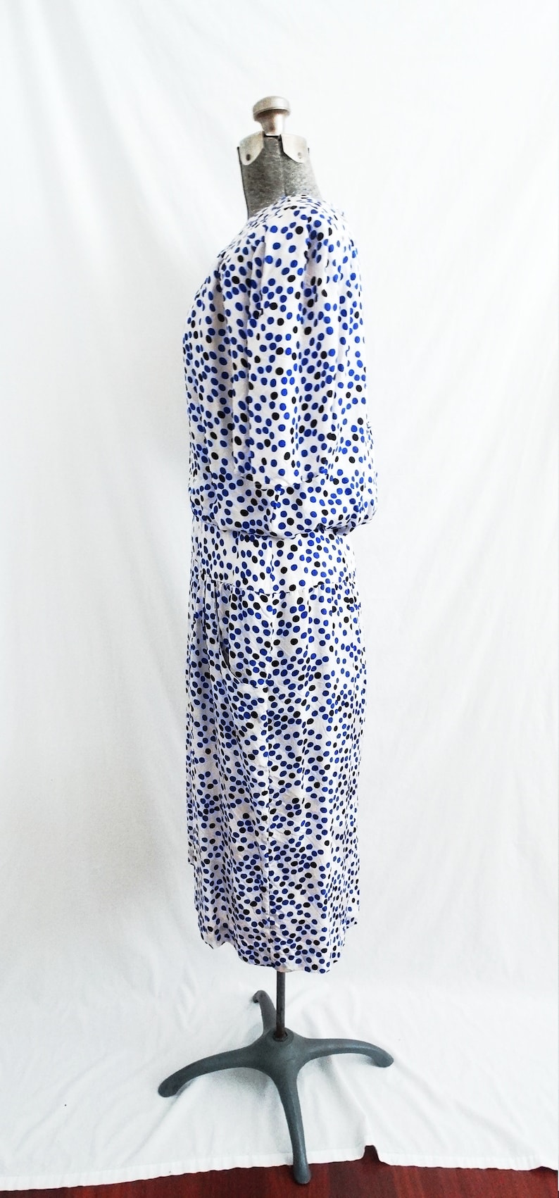 May include: A white dress with a blue and black polka dot pattern. The dress is on a mannequin and has a fitted bodice and a skirt that falls to the knees.