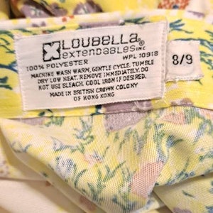 May include: A yellow and white floral fabric with a white tag that reads "Loubella extendables inc. WPL 10918 100% polyester Machine wash warm, gentle cycle. Tumble dry low heat. Remove immediately. Do not use bleach. Cool iron if desired. Made in British Crown Colony of Hong Kong 8/9"