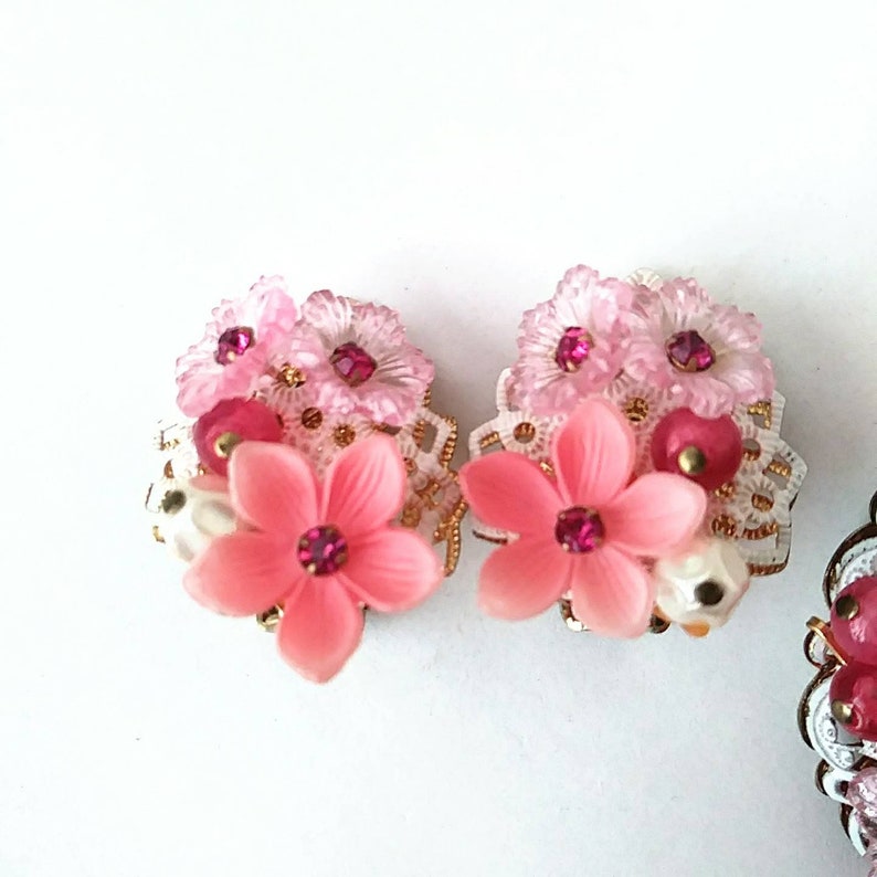May include: A pair of pink and white flower earrings with pink and gold accents. The earrings are made of polymer clay and feature a delicate lace design.