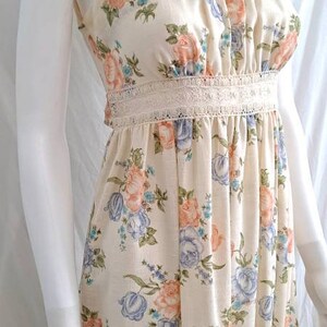 Puede incluir: Un vestido maxi sin mangas con estampado floral en tonos rosa, azul y verde. El vestido tiene un ribete de encaje blanco en el escote y la cintura.