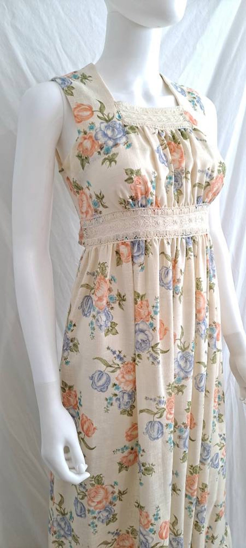 Puede incluir: Un vestido maxi sin mangas con estampado floral en tonos rosa, azul y verde. El vestido tiene un ribete de encaje blanco en el escote y la cintura.