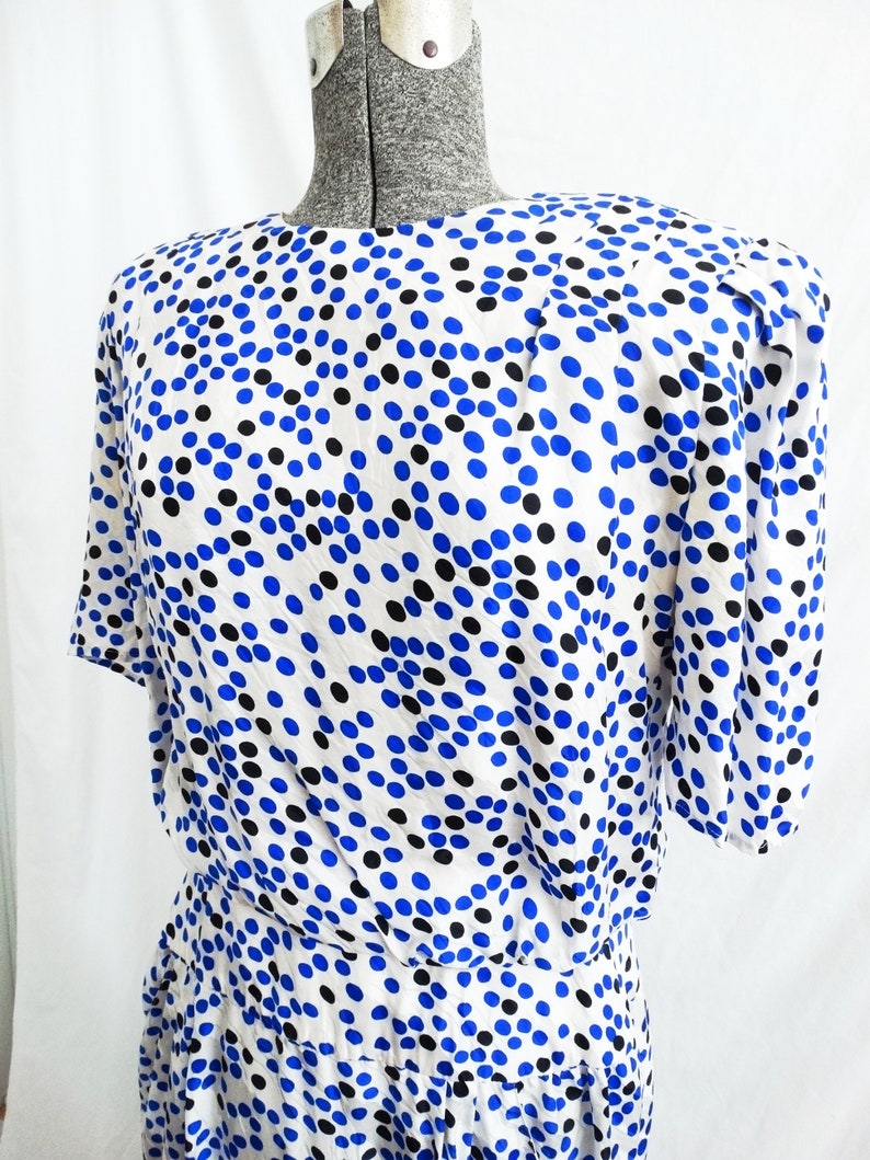 May include: A white dress with a blue and black polka dot pattern. The dress has short sleeves and a fitted bodice. The skirt is gathered and falls to the knees.