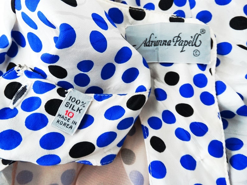 May include: White silk blouse with blue and black polka dots. The blouse has a label that reads "Adrianna Papell" and a tag that says "100% Silk, 10, Made in Korea."