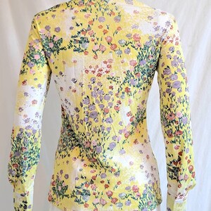 May include: A yellow long-sleeved shirt with a floral print. The shirt has a collared neckline and button closure. The flowers are in shades of pink, purple, and green.