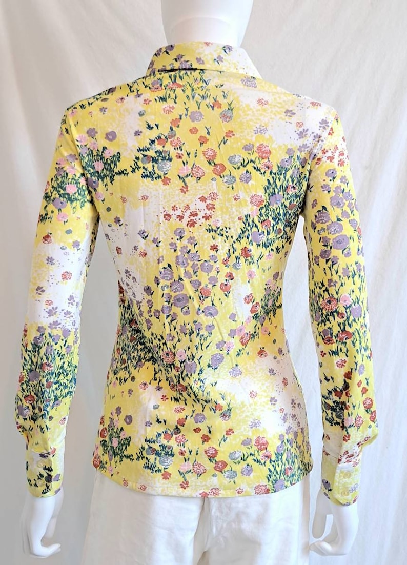 May include: A yellow long-sleeved shirt with a floral print. The shirt has a collared neckline and button closure. The flowers are in shades of pink, purple, and green.