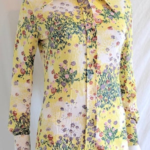 May include: A yellow long-sleeved button-up shirt with a floral print. The shirt has a wide collar and a button-up front.