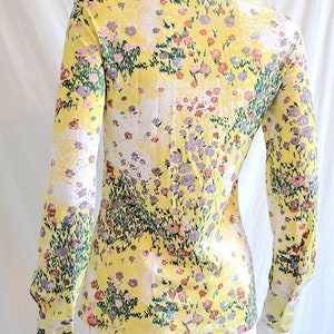 May include: A yellow long-sleeved shirt with a floral print. The shirt has a collared neckline and button closure. The print features a variety of flowers in shades of pink, purple, and green.