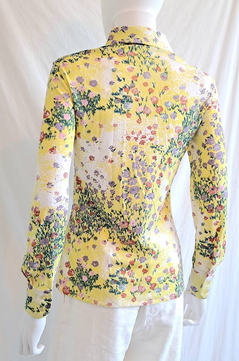 May include: A yellow long-sleeved shirt with a floral print. The shirt has a collared neckline and button closure. The print features a variety of flowers in shades of pink, purple, and green.
