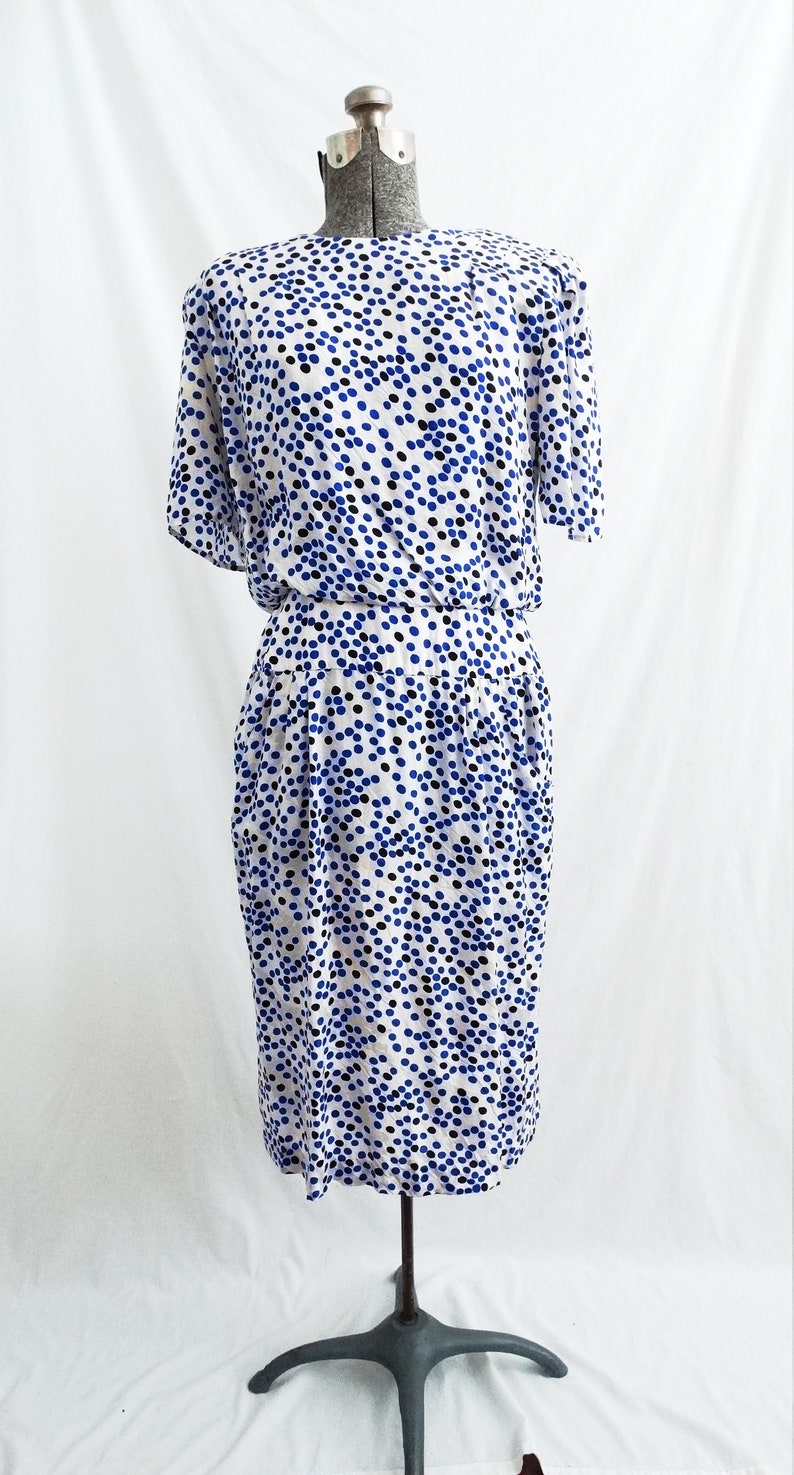 May include: A white dress with a blue and black polka dot pattern. The dress has a short sleeve and a fitted bodice. The skirt is slightly flared and falls to the knee.