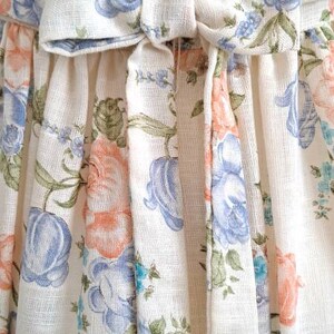 Puede incluir: Un vestido blanco con estampado floral con flores azules y rosas. El vestido tiene un lazo en la cintura.