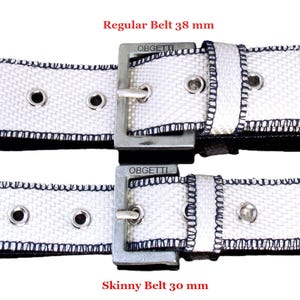 Può includere: Due cinture in tessuto bianco con fibbie argentate. La cintura superiore è etichettata "Regular Belt 38 mm" e la cintura inferiore è etichettata "Skinny Belt 30 mm".