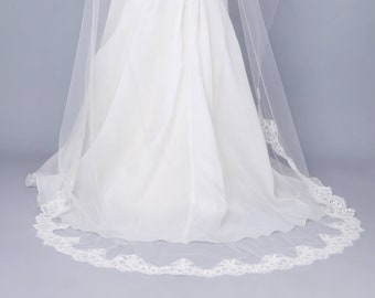 May include: A white bridal veil with a lace trim. The veil is long and flowing, and it is worn by a bride in a white wedding dress.