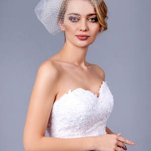 May include: A bride wearing a white strapless wedding dress with lace detailing and a white birdcage veil.