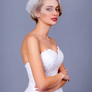 May include: A bride wearing a white strapless wedding dress with lace detailing and a white birdcage veil.