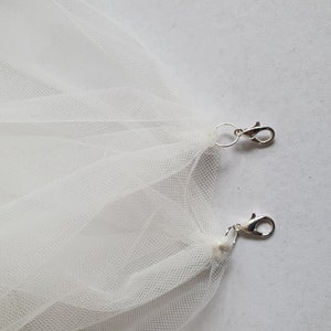 May include: Two silver clasps attached to a white tulle fabric.