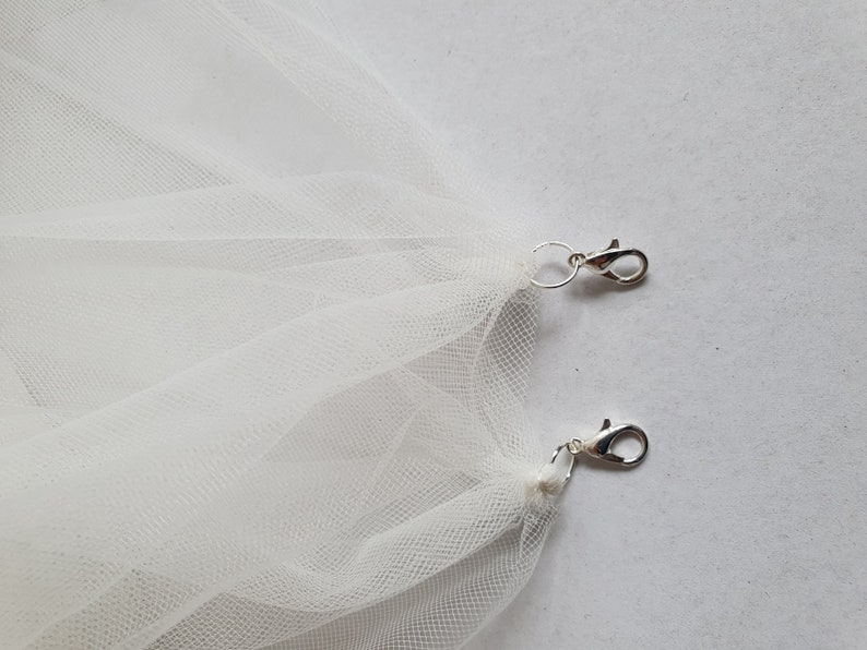 May include: Two silver clasps attached to a white tulle fabric.