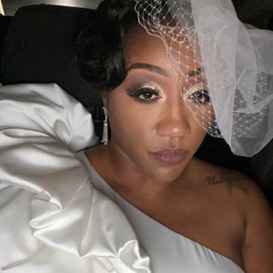 May include: A woman wearing a white one-shoulder dress with a veil and dramatic eye makeup.