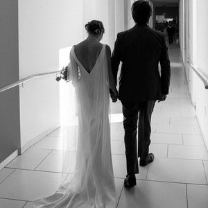 May include: A bride and groom in a white wedding dress and a black suit walk down a white tiled hallway.