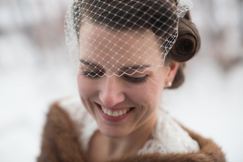 May include: A bride wearing a white veil with a brown fur shawl. She is smiling and looking down.