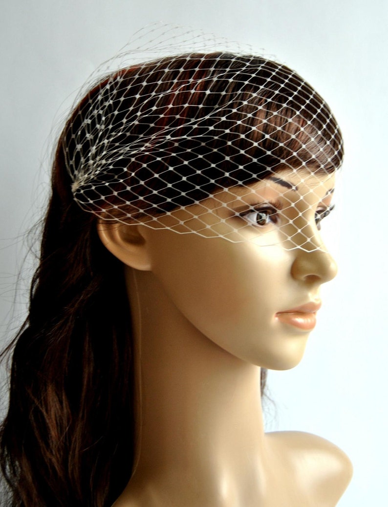 May include: A white bridal veil with a delicate net pattern. The veil is worn on a mannequin with long brown hair.