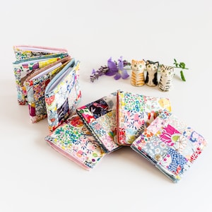 May include: A set of six colorful fabric covered notebooks with a patchwork design. The notebooks are arranged in a stack with the covers facing up. The notebooks are made of a variety of fabrics with floral and geometric patterns.