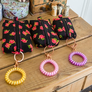 May include: Three black zippered pouches with a floral print and gold keychains with colorful spiral charms.
