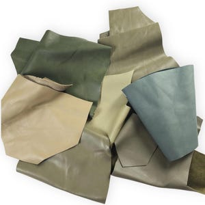May include: A collection of irregular leather scraps in various shades of green, olive, sage, and tan. The pieces feature smooth and textured surfaces with visible grain patterns, layered together to display a range of earthy, muted colour tones.