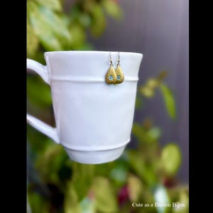 May include: A set of three ceramic mugs with a speckled, matte finish. The mugs are in shades of cream, light brown, and dark brown. Each mug has a simple, minimalist design and a rounded handle.