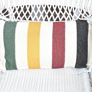 May include: A white wicker chair with a striped pillow. The pillow has green, yellow, red, and black stripes.