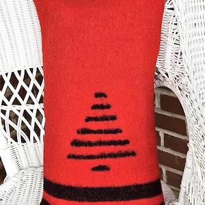 Op de afbeelding: Een rechthoekig rood kussen met een zwart boomontwerp en zwarte strepen aan de onderkant. Het kussen is gemaakt van een textuurrijk materiaal en ligt op een witte rotan stoel. Een decoratief woonaccessoire.