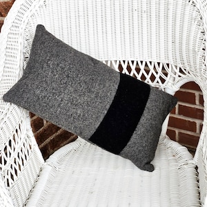 May include: A gray and black striped pillow sits on a white wicker chair. The pillow is made of a soft, fuzzy material.