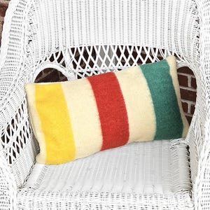 May include: A white wicker chair with a striped throw pillow. The pillow has yellow, white, red, and green stripes.