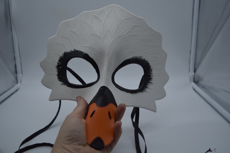 Op de afbeelding: Witte zwanenmasker met zwarte ooggaten en een oranje snavel. Het masker heeft een zwart elastisch bandje.