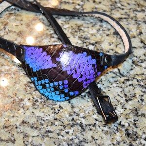 May include: A black leather eye patch with a blue, purple and black snakeskin pattern. The patch is attached to a black leather strap with a buckle.