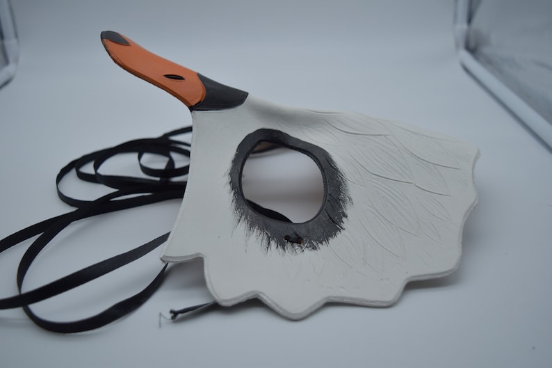 Op de afbeelding: Witte zwanenmasker met zwarte ooggaten en een oranje snavel. Het masker heeft een zwart lint om vast te binden.