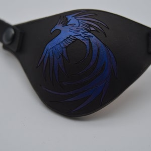Puede incluir: Parche para el ojo de cuero negro con un dise&ntilde;o de f&eacute;nix azul y morado.