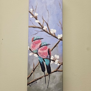 May include: A painting of two pink and blue birds perched on a branch with white blossoms. The background is a light blue sky. The painting is signed "D.Revete" in the lower right corner.