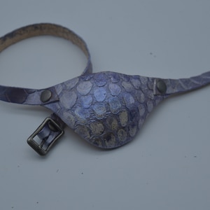 May include: A purple leather eye patch with a buckle strap. The patch has a textured, scaly design.