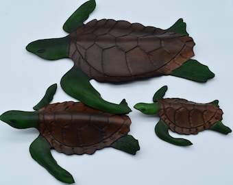 Könnte beinhalten: Drei Wandskulpturen von Lederschildkröten in verschiedenen Größen. Die Schildkröten sind braun mit grünen Flossen und Köpfen.