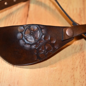May include: A brown leather steampunk eye patch with two gear designs embossed on the front. The patch has a copper coloured button on the strap.