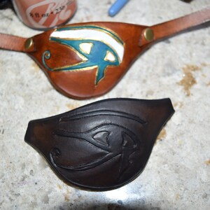 Op de afbeelding: Twee leren ooglapjes met een Egyptisch oog van Horus-ontwerp. E&eacute;n is bruin met een blauw en gouden oog, de andere is zwart met een zwart oog.