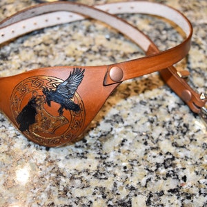 May include: A brown leather eye patch with a Celtic knot design and two black ravens. The eye patch has a brown leather strap with a silver buckle.