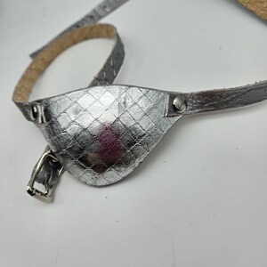 May include: A silver leather eye patch with a strap. The patch has a textured, diamond-shaped pattern.