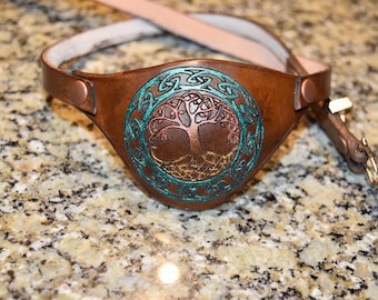 Könnte beinhalten: Ein braunes Leder-Augenpflaster mit einem keltischen Knotendesign und einem Lebensbaummotiv in Türkis, Gold und Kupfer.